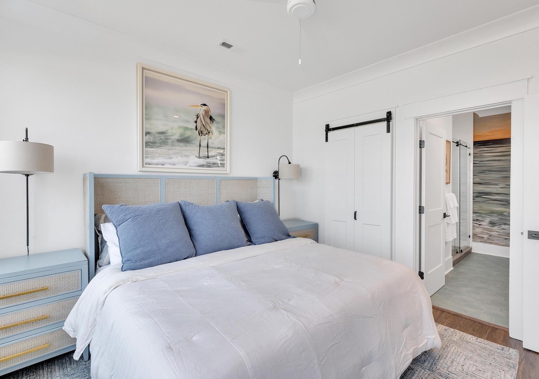 Your bright coastal bedroom features crisp linens, serene blue accents, and a charming barn door leading to your private ensuite—where peaceful relaxation awaits.