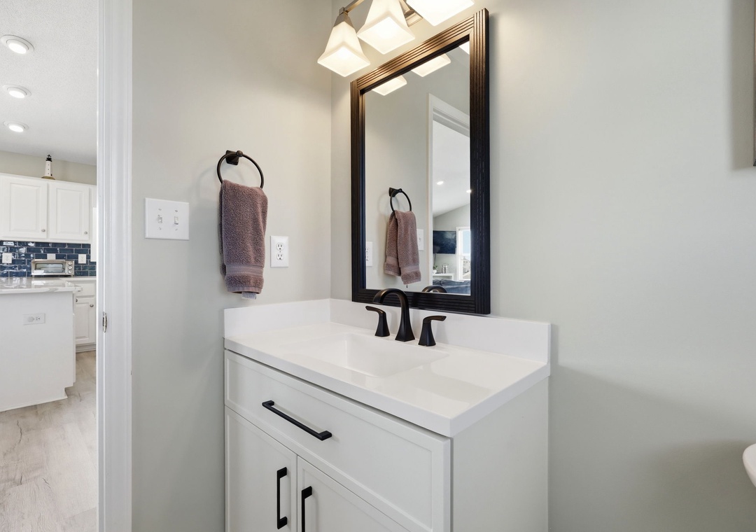 Freshen up in your stylish bathroom featuring a crisp white vanity, framed mirror, and modern fixtures. Soft lighting and thoughtfully placed towels create a welcoming retreat.