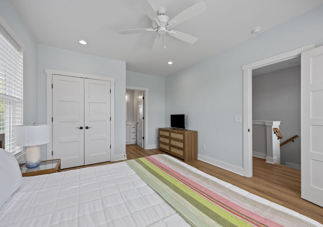 Your airy bedroom features bright natural light, a ceiling fan for comfort, and a colorful striped rug adding warmth to the clean design.