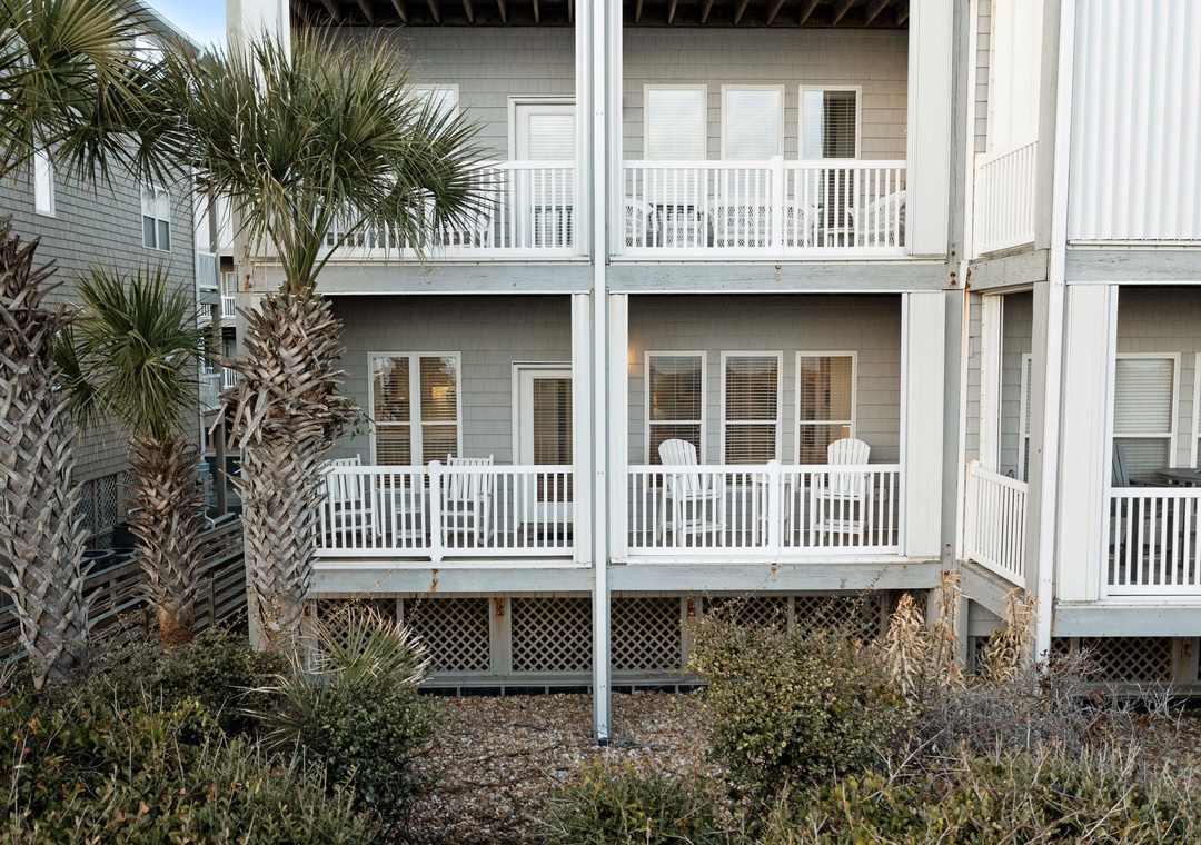 Coastal vacation rental with palm trees and private balconies featuring outdoor seating in a peaceful beachside setting.