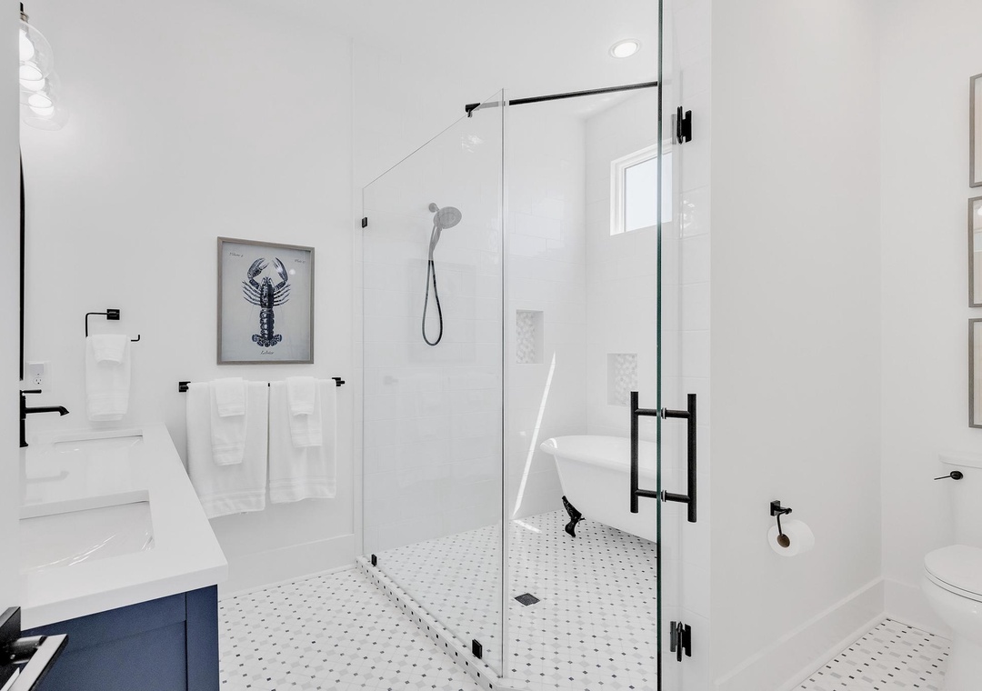 Step into your serene spa-like bathroom featuring a spacious glass-enclosed shower, crisp white finishes, and charming coastal artwork to refresh your senses.