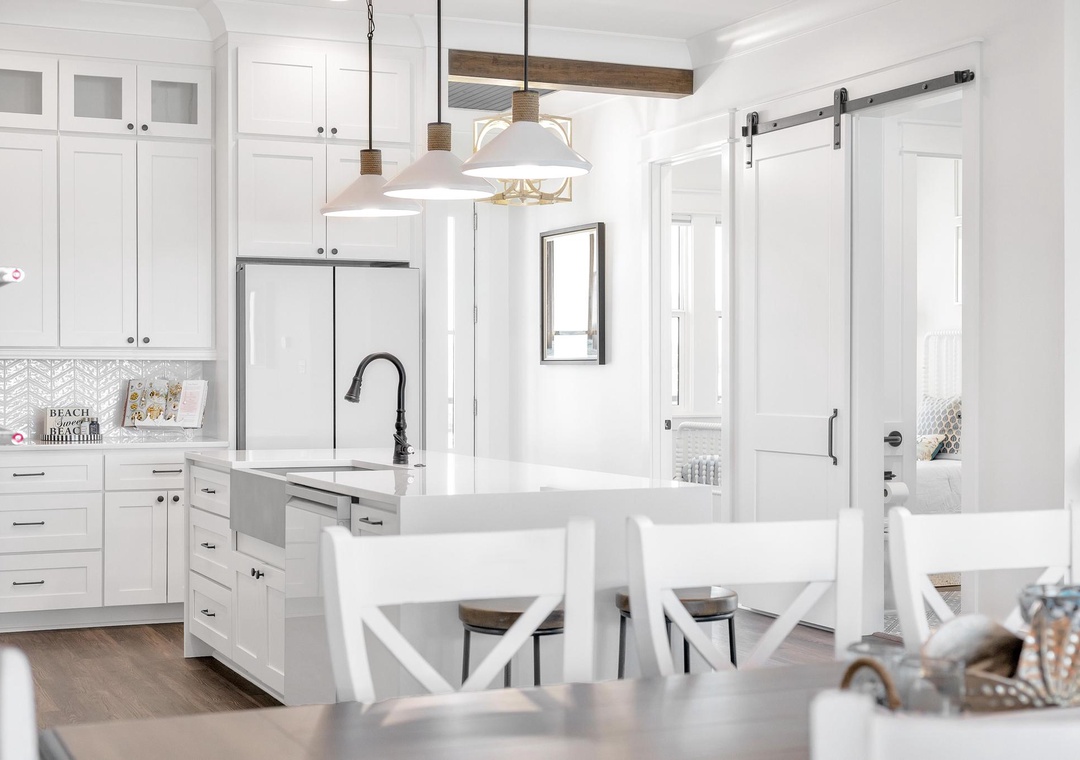 Bright, open kitchen with modern appliances, pendant lighting, and a charming barn door inviting you to relax and cook your favorite meals in this airy coastal space.