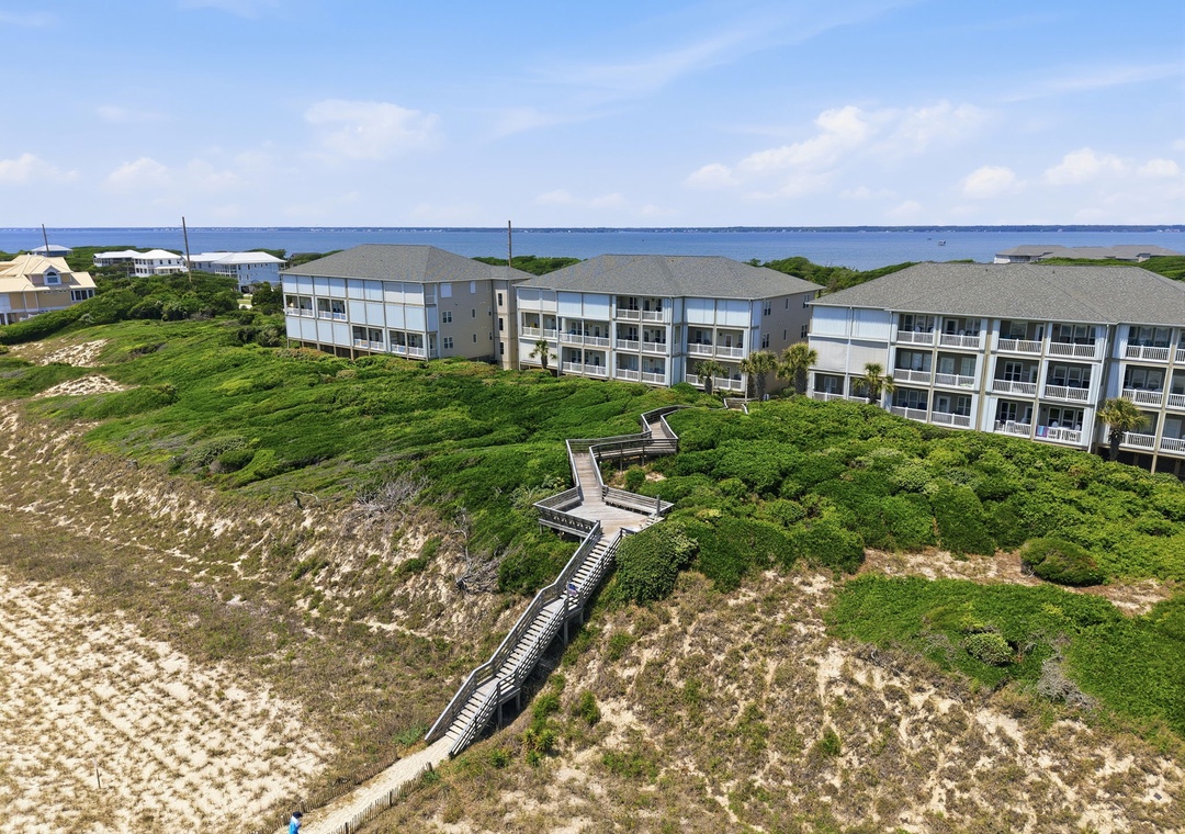 Aerial view of a beachfront vacation property with direct ocean access via elevated wooden walkways, nestled among lush coastal dunes and natural vegetation.