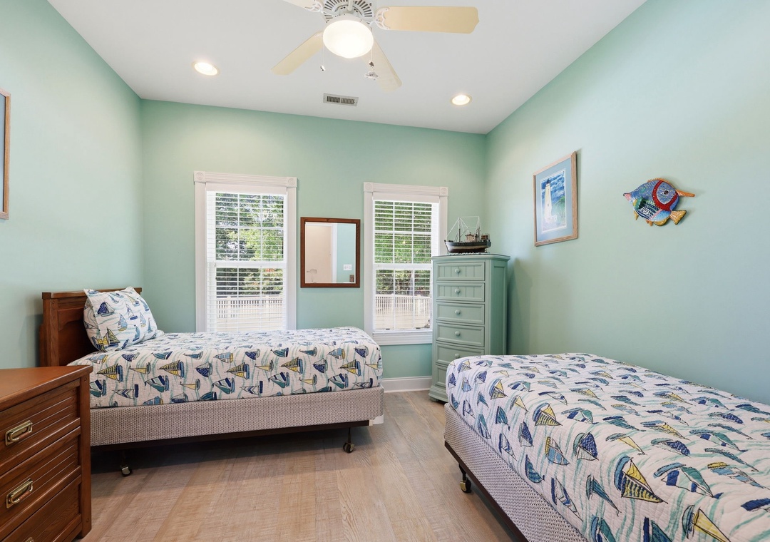 Relax in your breezy coastal bedroom with twin beds, ceiling fan, and cheerful nautical touches. Natural light fills the space with a welcoming, airy feel.