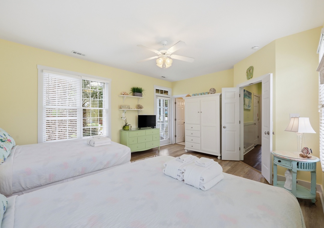 Unwind in your cheerful, sunlit bedroom with two cozy beds, ceiling fan, and ensuite bath. Fresh towels await you, and bright windows frame your peaceful retreat.