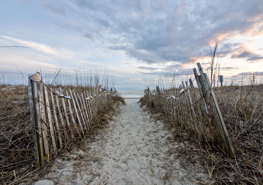 A scenic boardwalk path leads through coastal dunes to the pristine beach beyond, offering peaceful access to the shore.