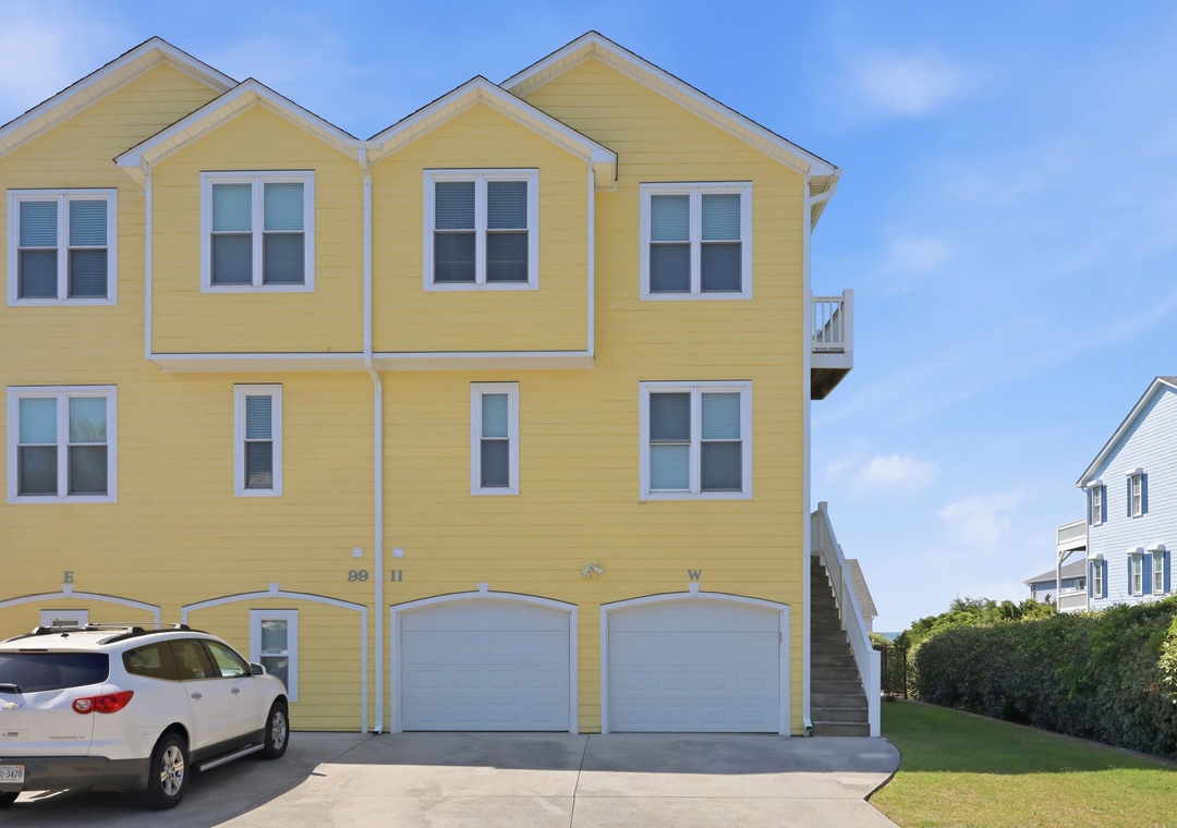 Cheerful yellow multi-unit beach property features ample parking and private garages, with an outdoor stairway leading to upper-level accommodations and nearby coastal access.