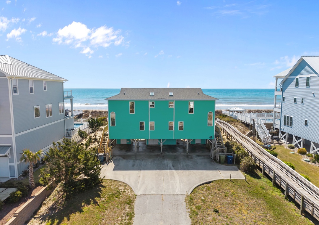 Bright turquoise beach house with ocean access, elevated on stilts with ample parking and boardwalk leading to pristine sandy shores.