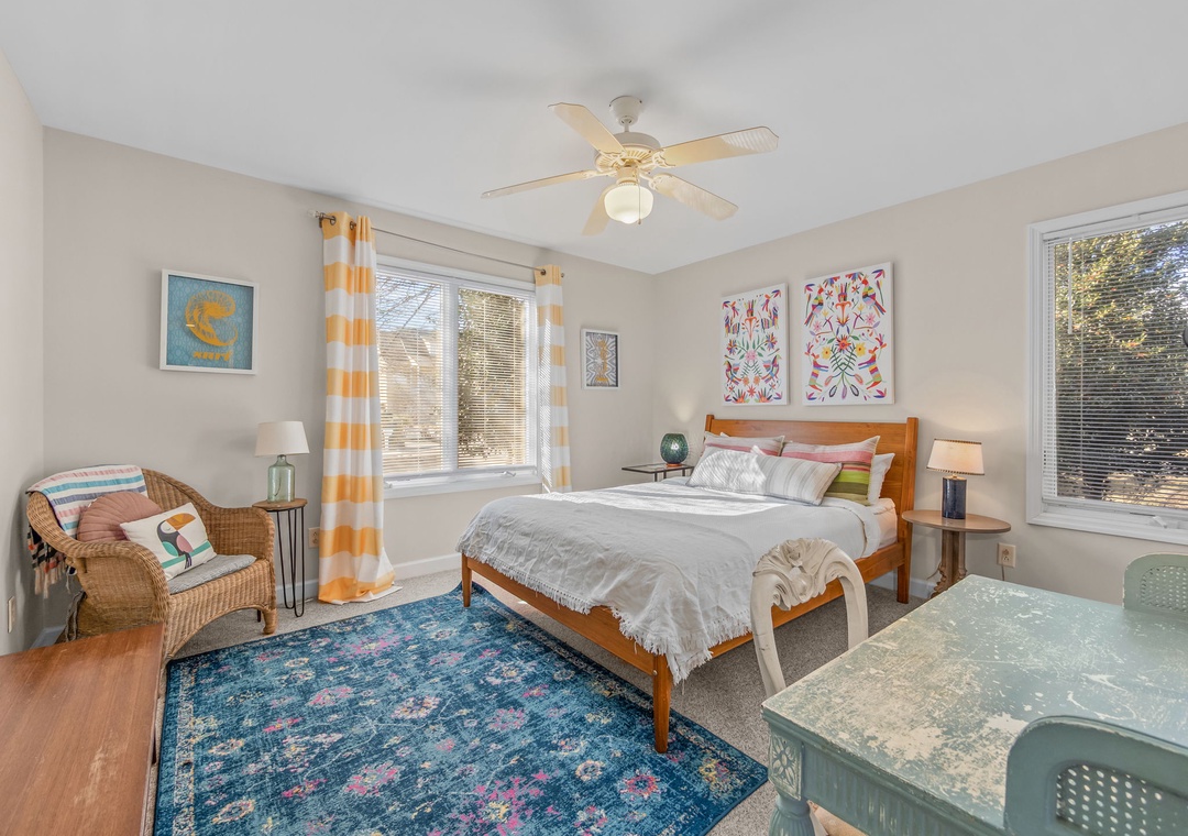 Sink into comfort in your bright bedroom featuring cheerful artwork, cozy seating, and windows that fill the space with natural light.