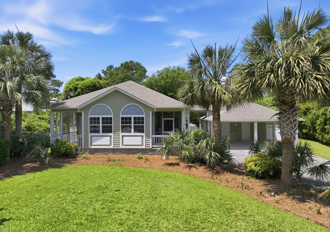 A charming single-story coastal home nestled among palm trees and lush greenery, offering a peaceful retreat with a screened porch and covered parking in a quiet neighborhood setting.