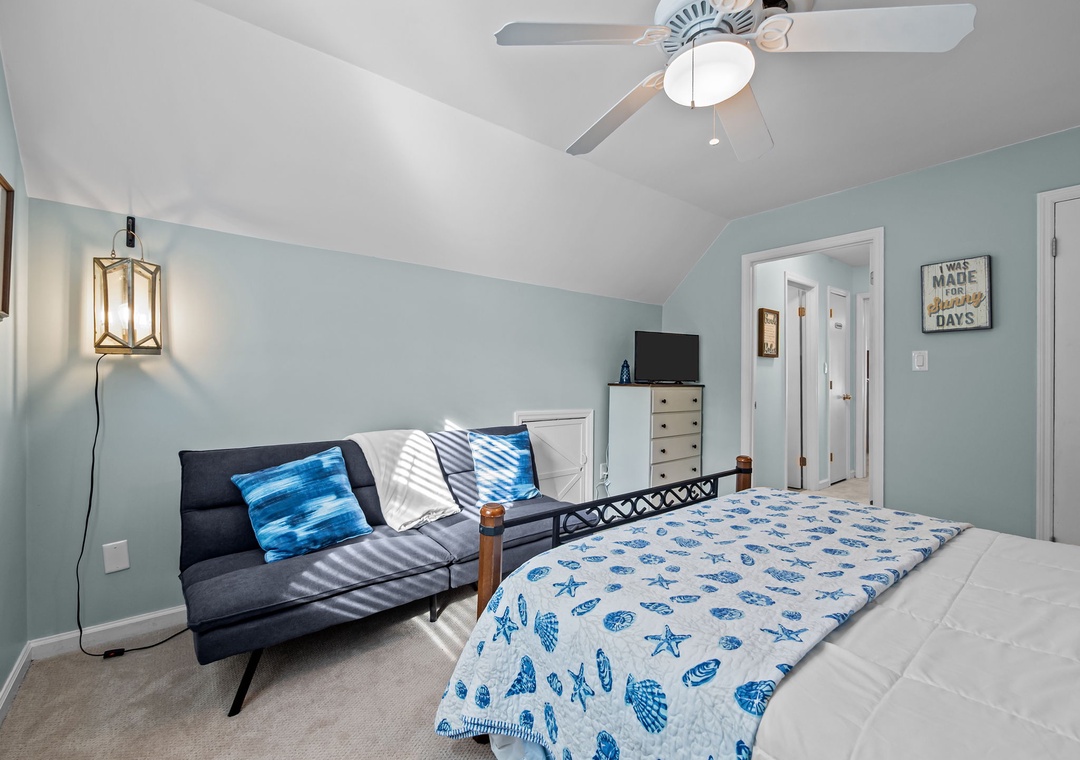 Drift off in this coastal-themed bedroom with soothing blue accents, comfortable seating area, and gentle ceiling fan for peaceful nights.