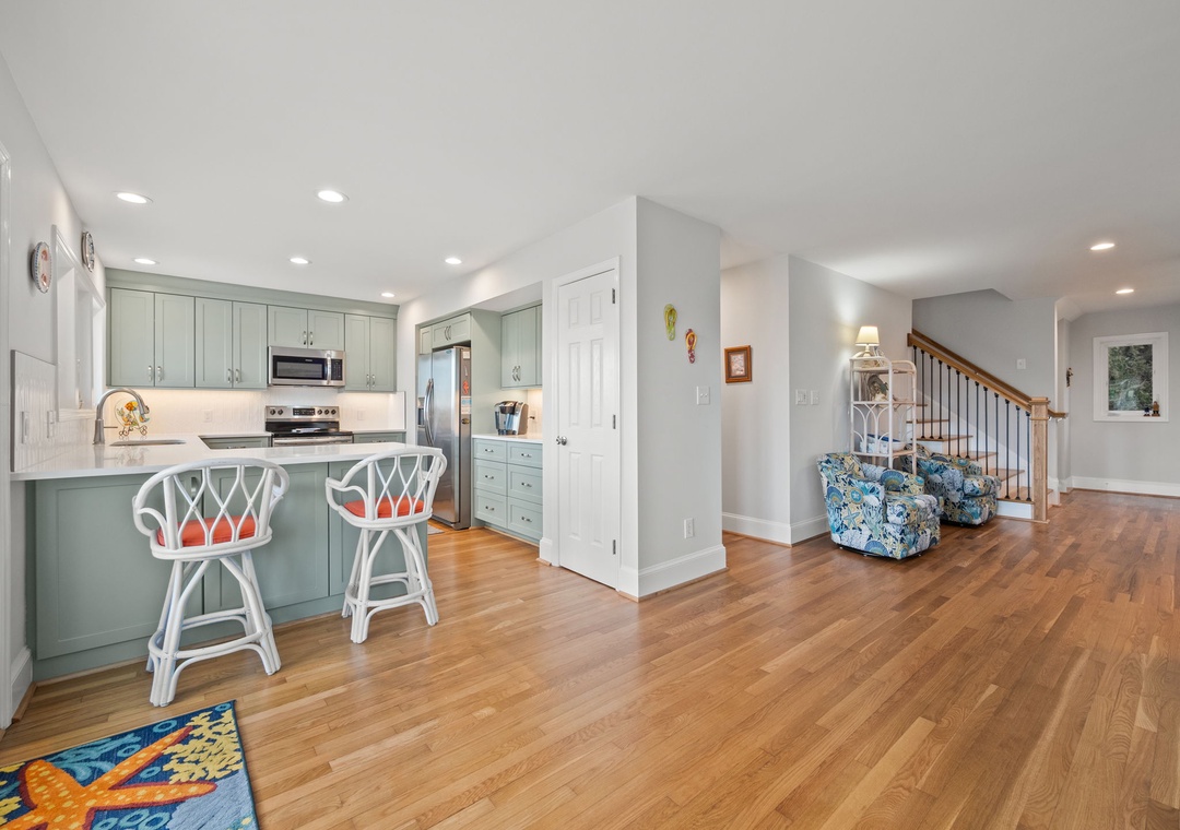 Your open-concept kitchen flows seamlessly into the living area, featuring sage green cabinets and gleaming hardwood floors throughout.
