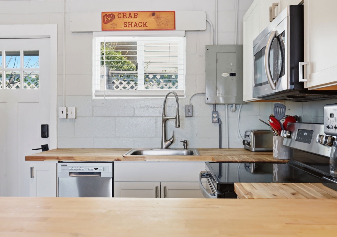 Your fully equipped kitchen features modern appliances, butcher-block counters, and charming coastal character with a cheerful 'Crab Shack' sign overhead welcoming you to cook and gather.