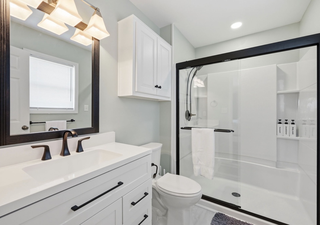 Step into a spotless bathroom with modern fixtures, soft lighting, and a spacious walk-in shower. White cabinetry offers plenty of storage, while natural light from the window enhances your morning routine.