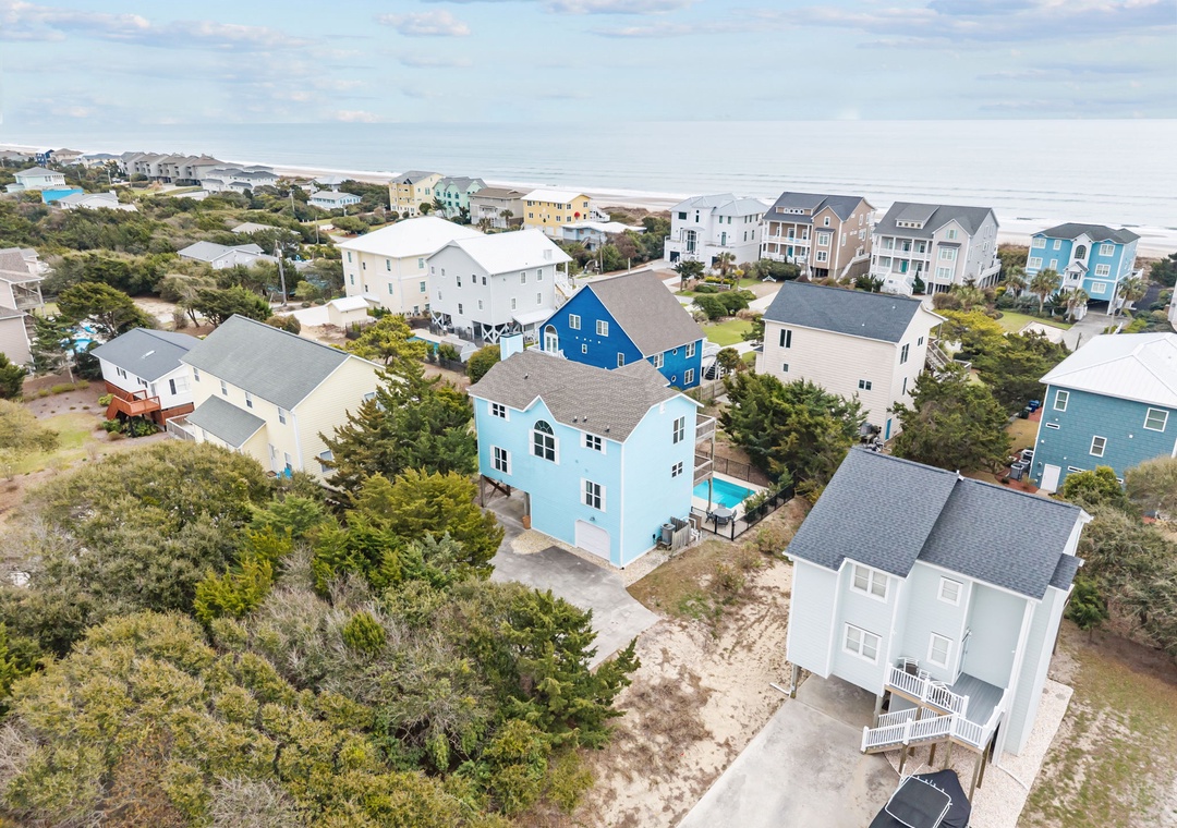 Aerial view of a charming coastal neighborhood with colorful beach houses nestled among natural vegetation near the shoreline.