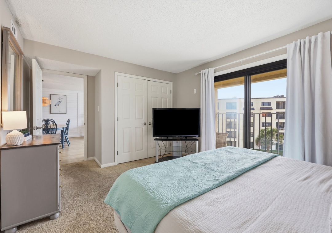 Settle into your serene bedroom where soft linens and calming coastal colors invite relaxation, while your private balcony frames peaceful city views beyond crisp white curtains.