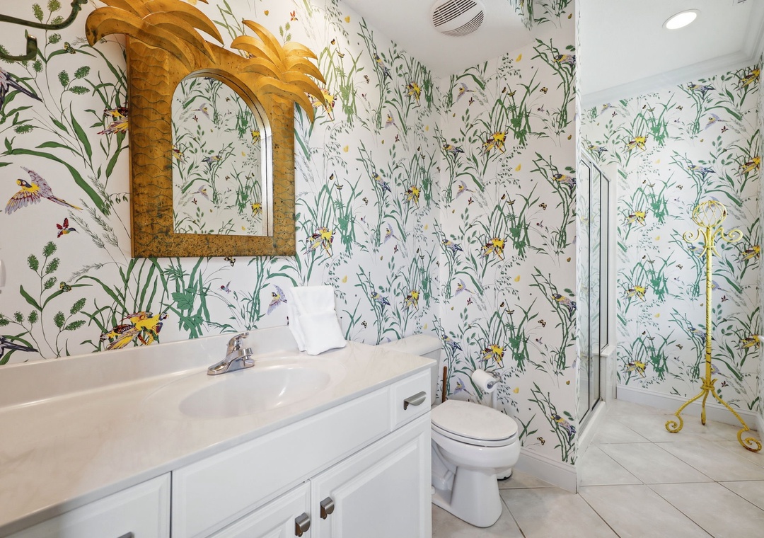 A vibrant botanical-themed bathroom featuring whimsical wallpaper with birds and florals, a golden palm mirror, and a cheerful atmosphere that makes freshening up feel like a tropical escape.