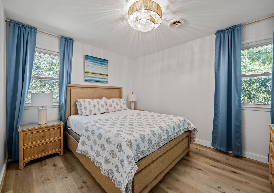 Your peaceful bedroom features warm wood furnishings and soft blue accents, with natural light streaming through dual windows for restful mornings.