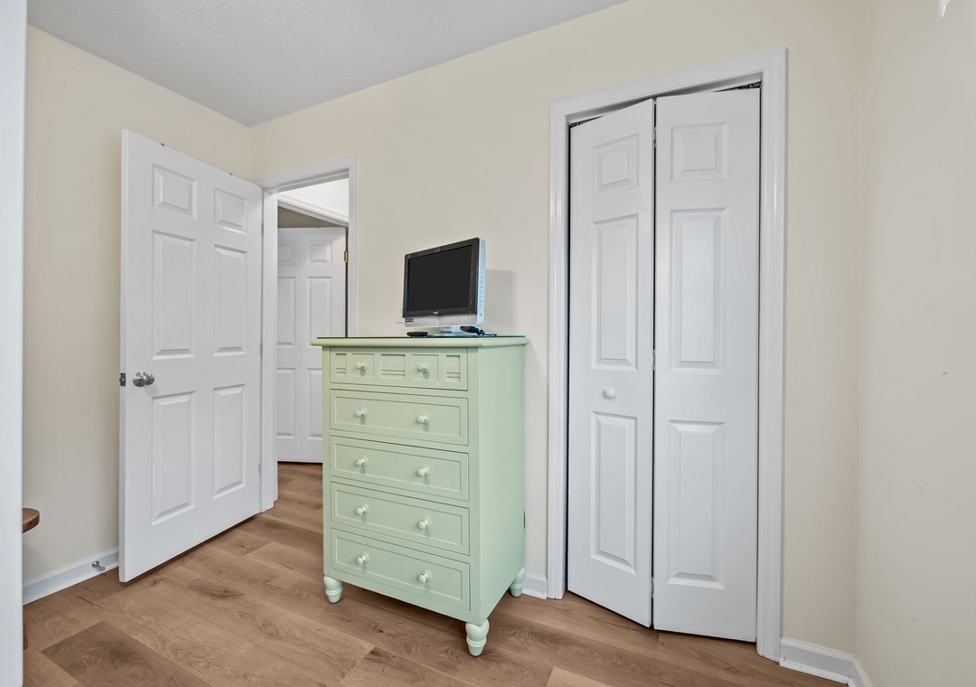 Unpack your belongings in this charming bedroom corner with ample storage in the mint-green dresser and convenient TV for evening relaxation.