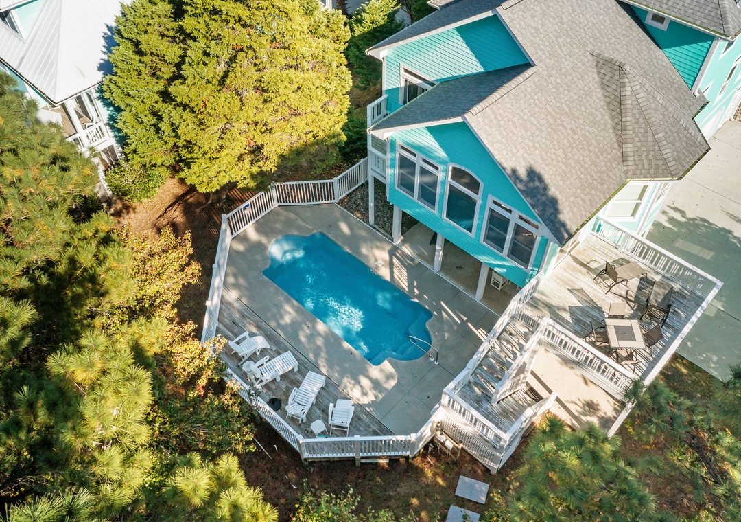 Aerial view of a vibrant turquoise beach house surrounded by lush landscaping and featuring a private swimming pool with multi-level deck areas.