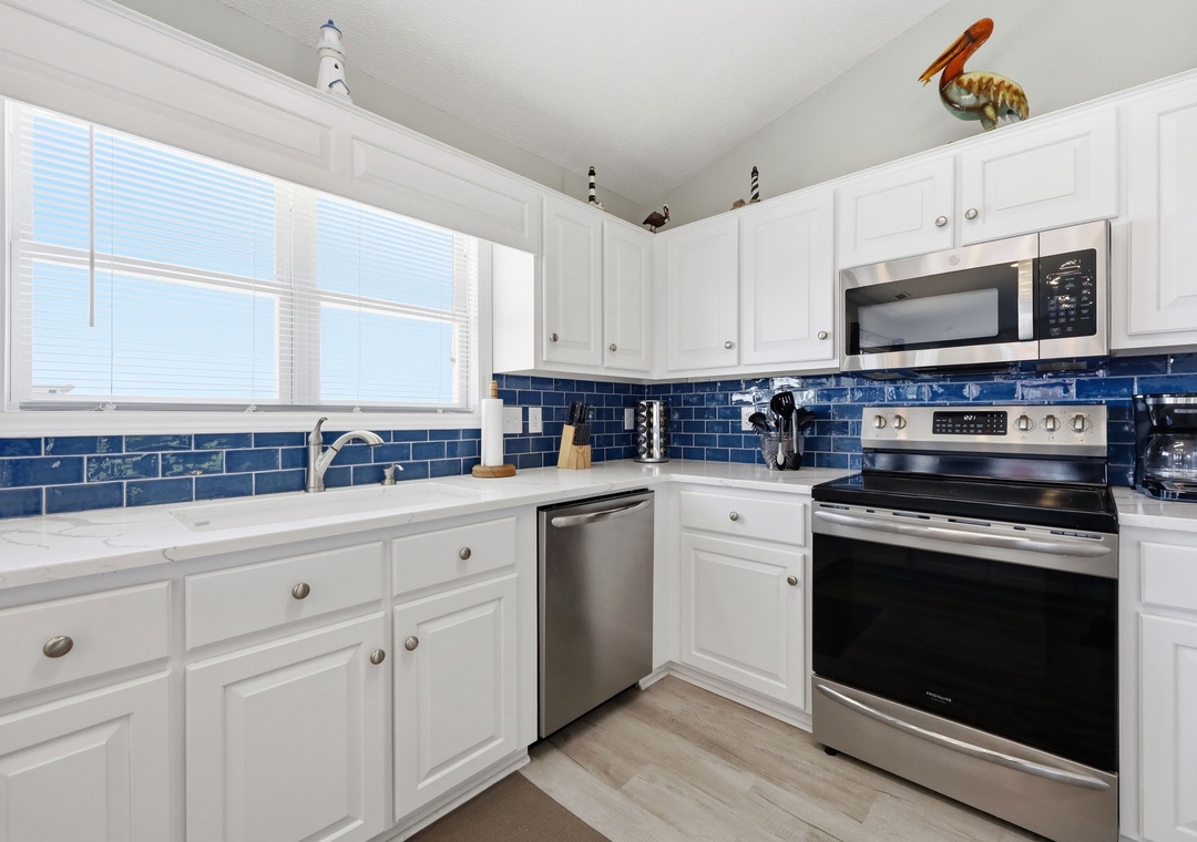 This bright, coastal-inspired kitchen features crisp white cabinetry, gleaming stainless steel appliances, and charming blue subway tile backsplash that brings the beach home with you.