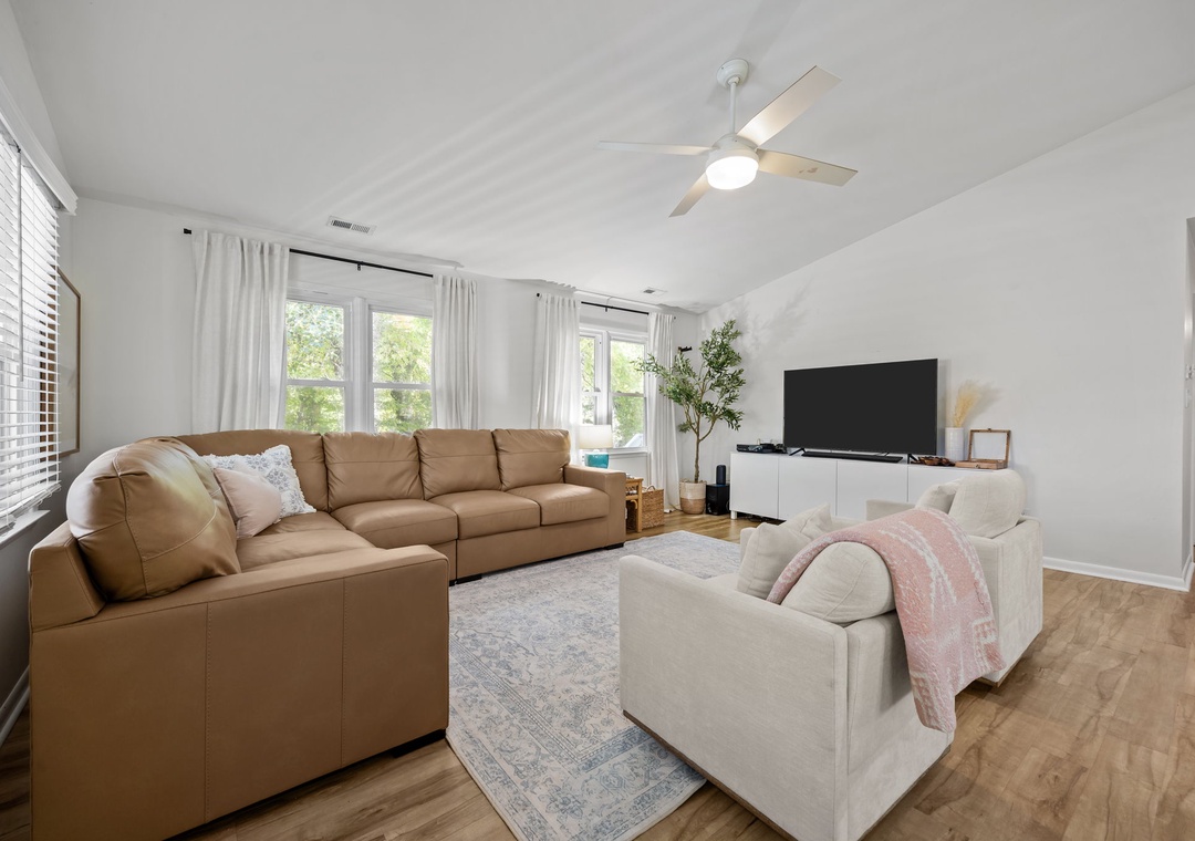 Relax in your bright, open living room with plush seating, modern entertainment center, and ceiling fan keeping you comfortable all day.