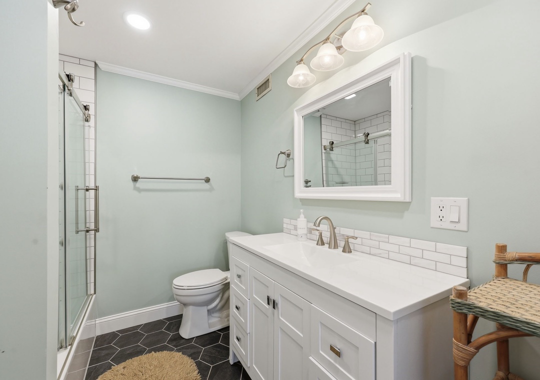 Step into your beautifully renovated bathroom featuring soft mint walls, crisp white subway tile, and a sleek glass-enclosed shower. The spacious vanity provides plenty of room to refresh and unwind after a day of exploring.