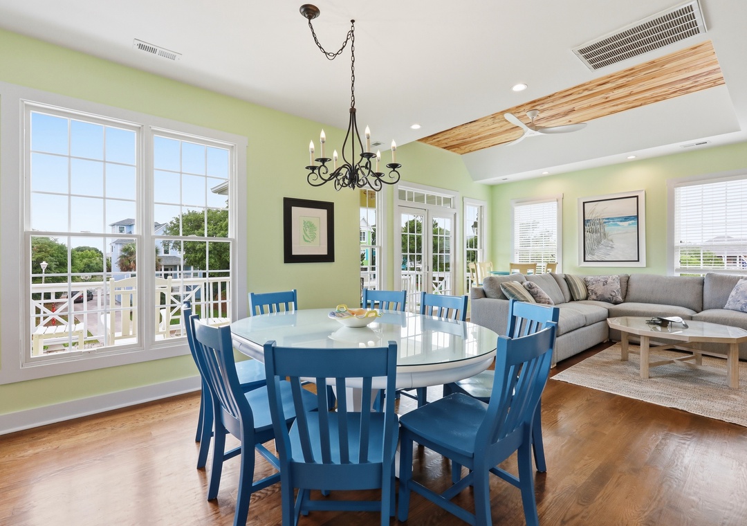 Gather around this bright dining space where coastal charm meets comfort. Soft green walls and ocean-inspired décor invite you to share meals while natural light floods in through large windows overlooking the neighborhood.