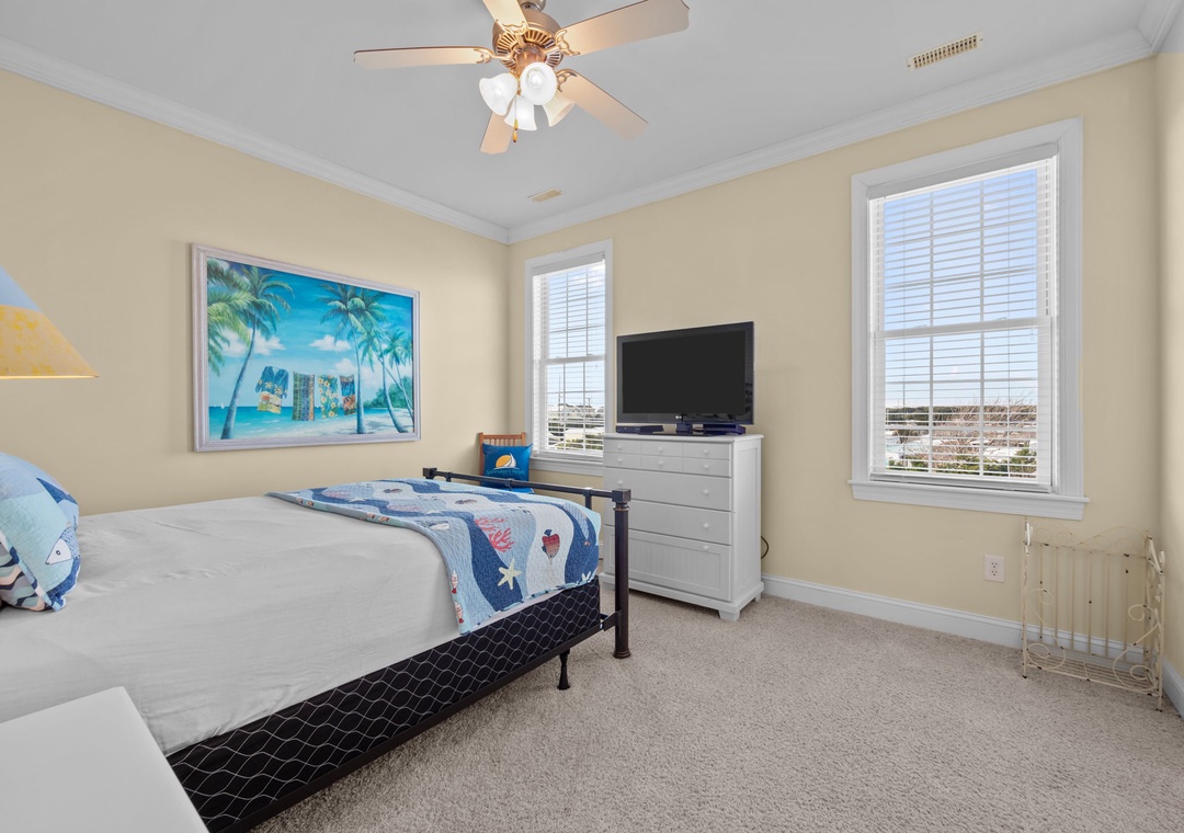 Drift off in this bright bedroom with ocean artwork, TV, and ceiling fan for your comfort.