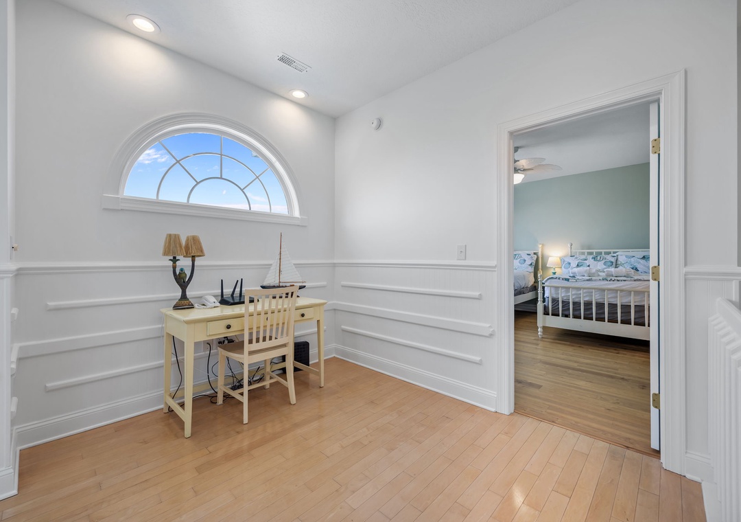 Your bright workspace awaits with elegant wainscoting, an arched window, and polished hardwood floors perfect for peaceful productivity.