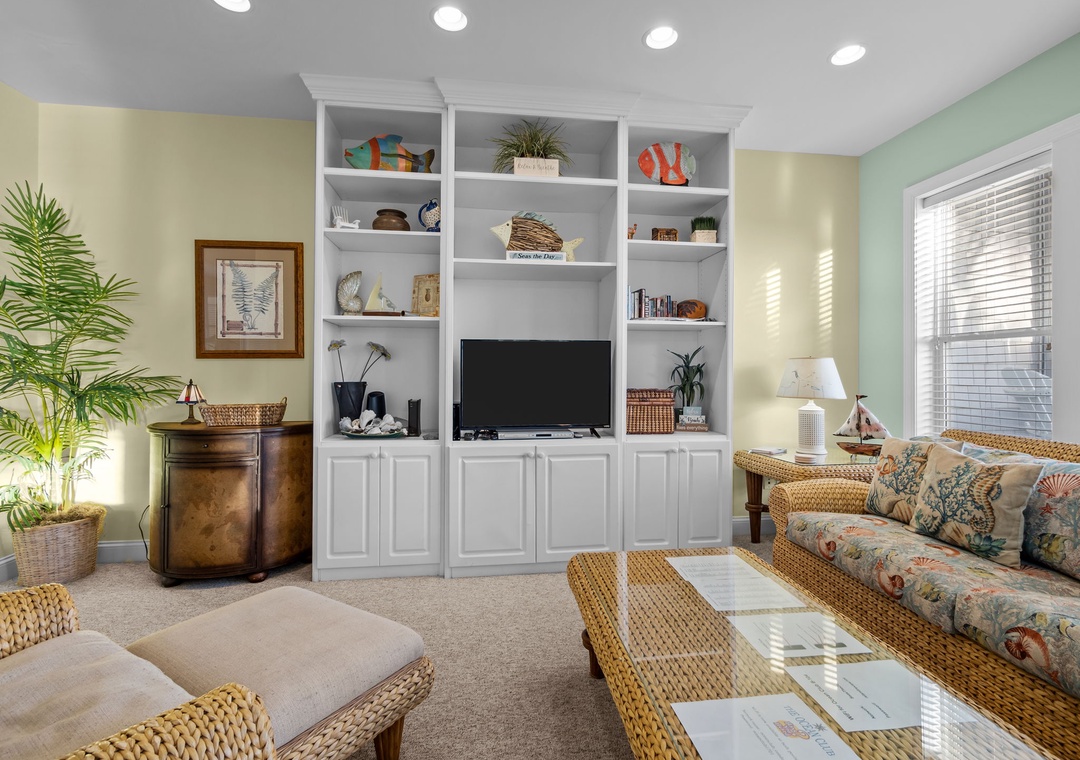 Relax in this bright living space featuring coastal charm with wicker furniture, built-in entertainment center, and tropical plants creating your perfect beach getaway.