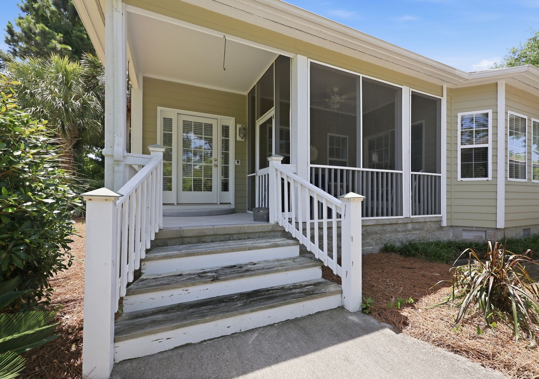 The property entrance features a charming screened porch and white wooden stairs, surrounded by lush tropical landscaping that creates a welcoming arrival experience.