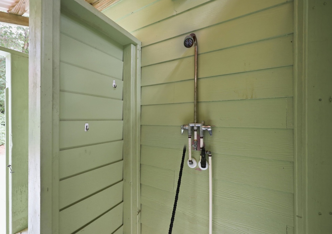 An outdoor shower is surrounded by green wooden paneling. This property includes an accessible outdoor rinse station for refreshing after beach visits or outdoor adventures.