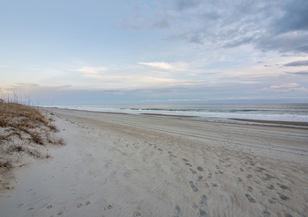 Pristine coastal beach with soft sand dunes and gentle waves under a dramatic cloudy sky.