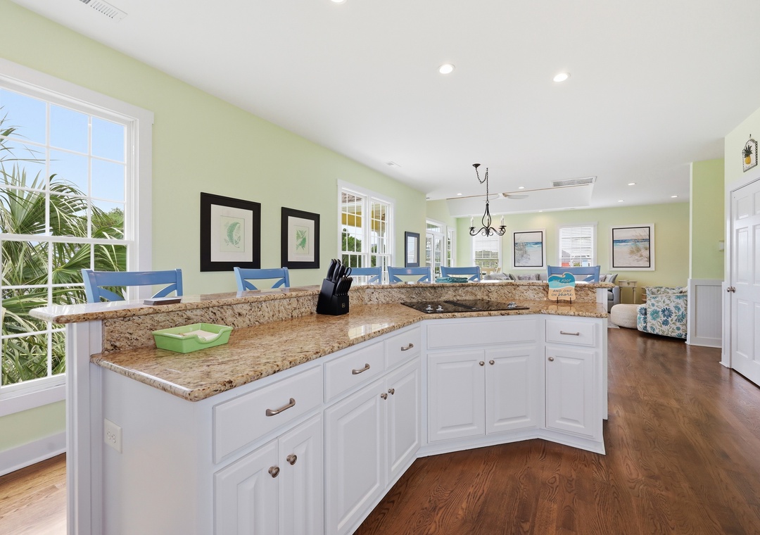 Prepare meals in your sunlit kitchen with granite countertops and white cabinetry, with tropical views through large windows and a welcoming open layout flowing into the living space.