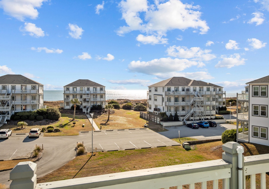 Oceanfront vacation community with multi-story beach houses, parking areas, and direct beach access under bright blue skies.