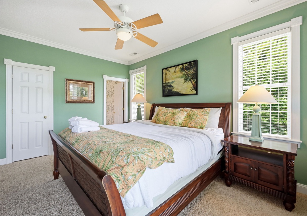 Sink into crisp white linens and tropical comfort in your serene bedroom, where gentle breezes from the ceiling fan and soft natural light create the perfect retreat for restful nights.