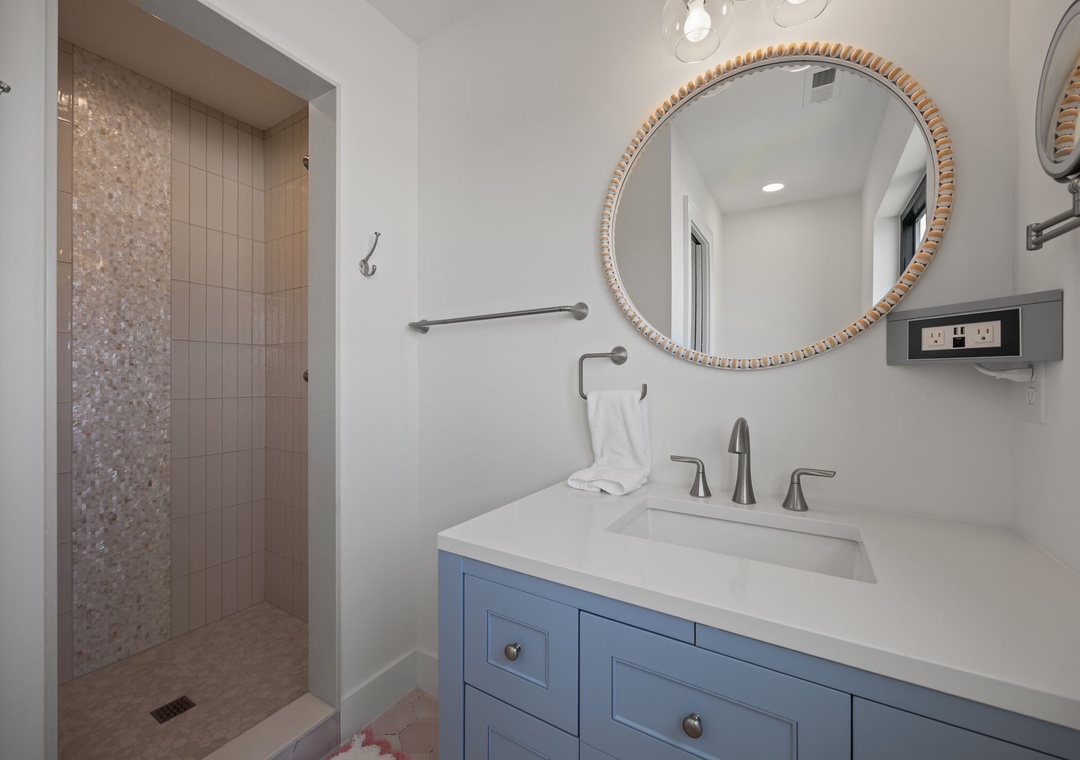 Refresh in your elegant ensuite with marble countertops, stylish blue vanity, and luxurious walk-in shower featuring stunning mosaic details.