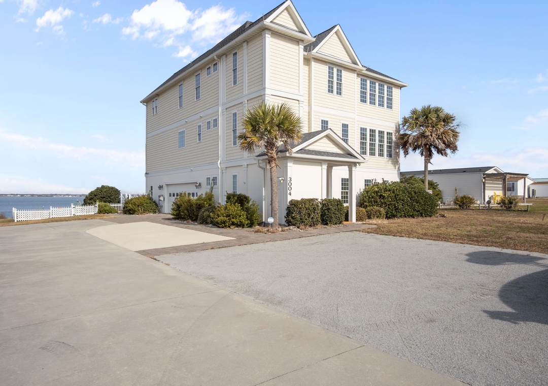 Spacious three-story coastal home with palm trees and ample parking, perfectly positioned in a quiet residential setting.