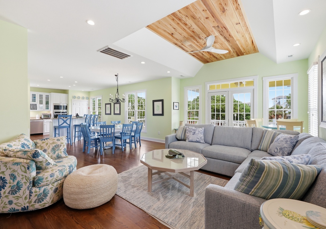 Relax in your bright, open living space featuring vaulted ceilings with warm wood accents, plush seating, and cheerful coastal decor—perfect for gathering with family or unwinding after a beach day.