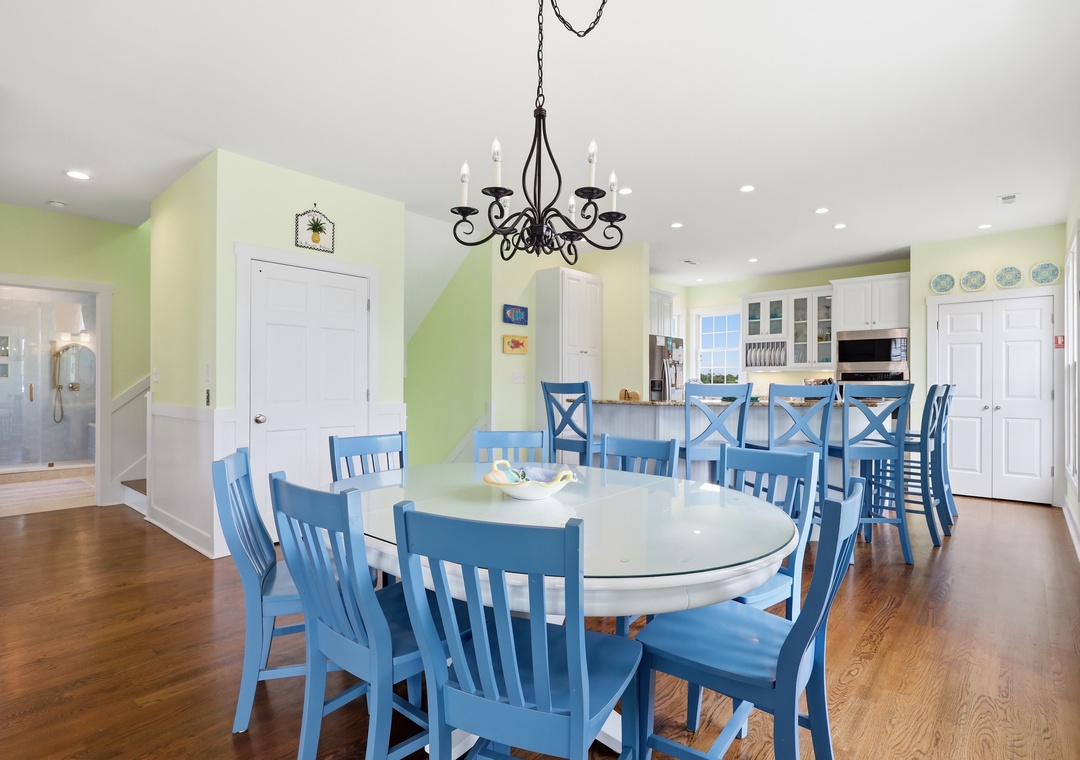 Gather around the spacious dining table with seating for twelve, where laughter flows freely under the warm chandelier glow. The open kitchen invites you to whip up feasts together in this bright, cheerful space.