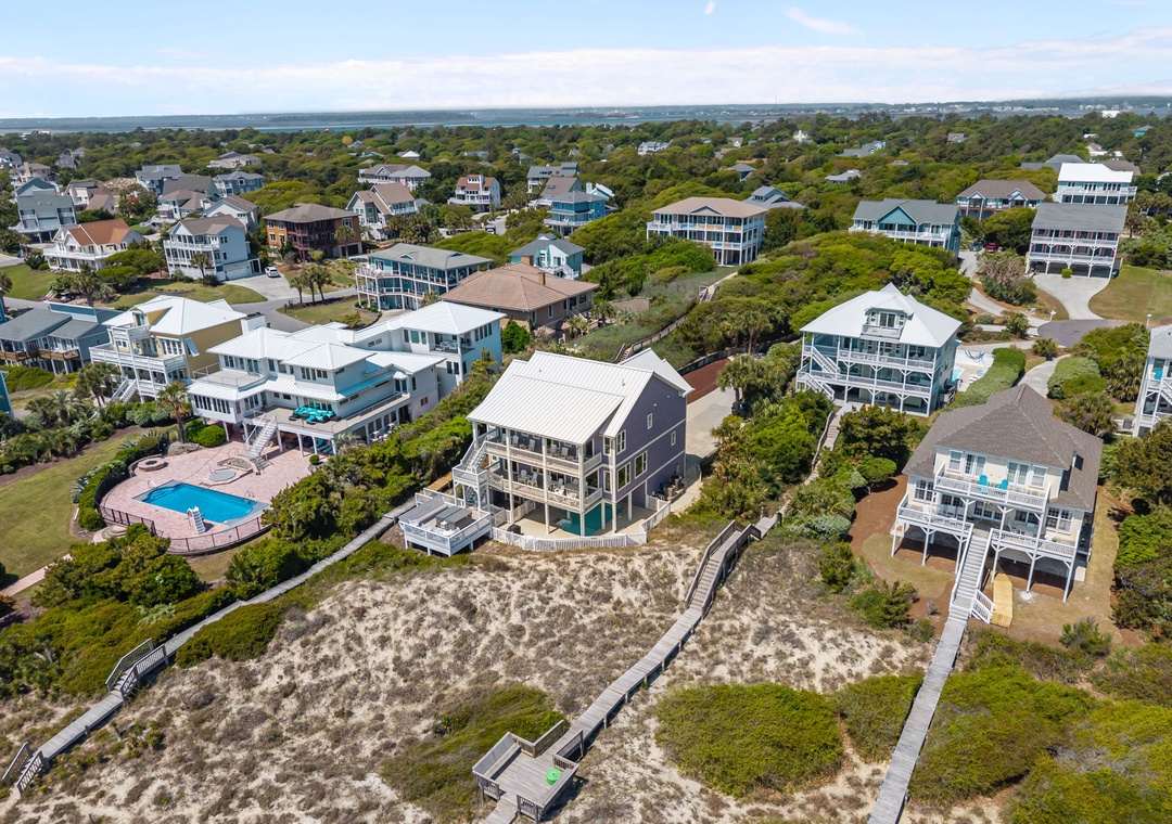 Aerial view of coastal vacation homes nestled among lush vegetation, featuring a mix of traditional and modern architecture with ocean access via wooden boardwalks.