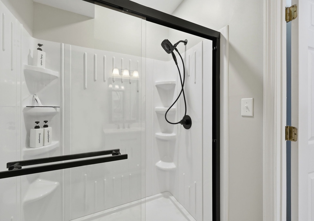 Step into your pristine, modern shower featuring elegant black fixtures, built-in shelving for your essentials, and a rainfall showerhead for a refreshing start to your day.