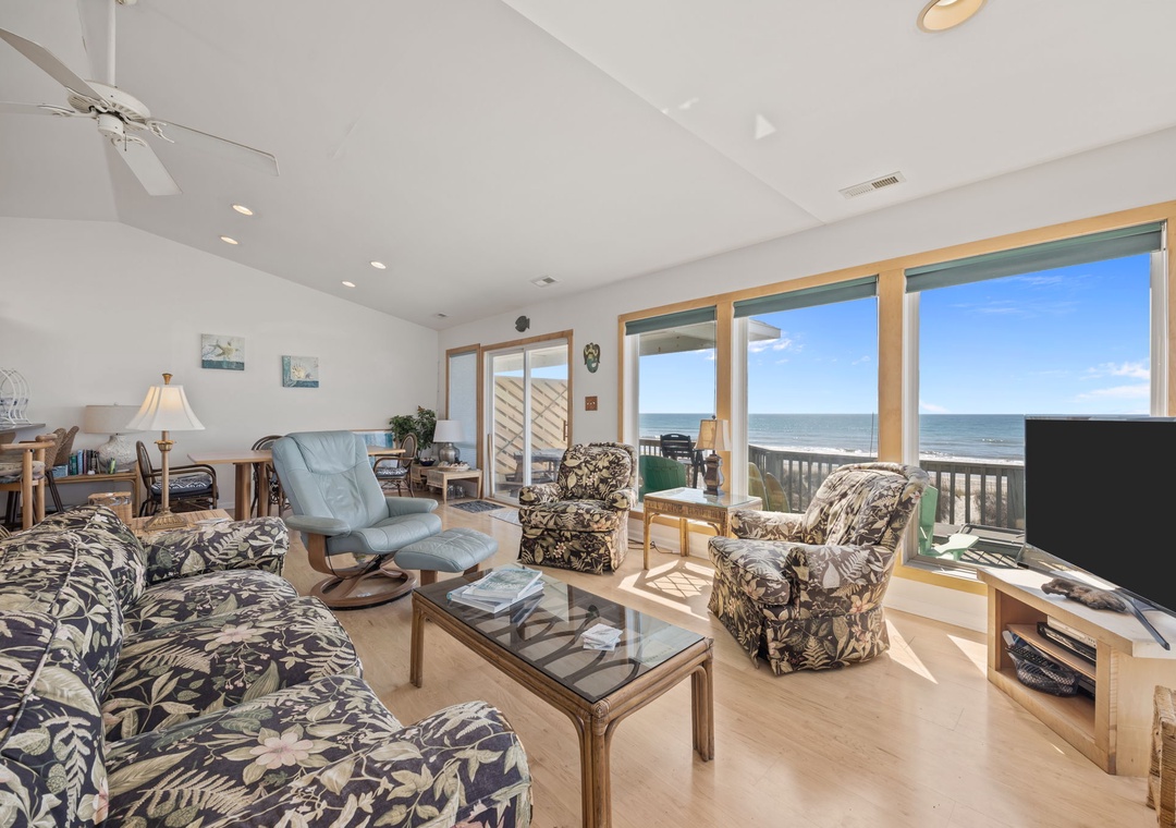 Relax in your bright oceanfront living room where comfortable seating meets stunning sea views through expansive windows.