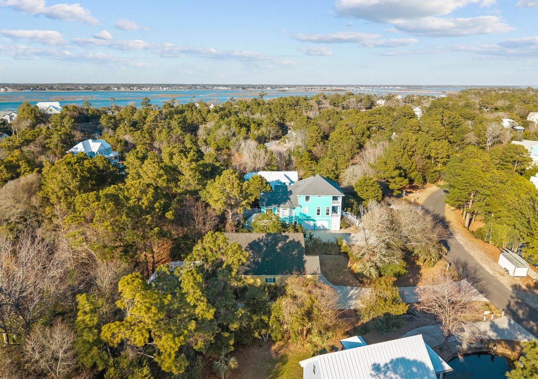 Aerial view of a charming coastal property nestled among mature trees with the sparkling waterfront just beyond.