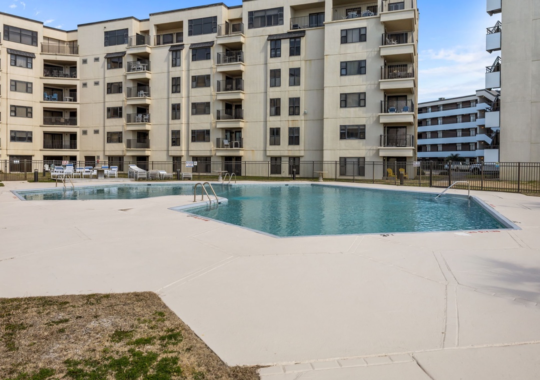 Multi-level property featuring a sparkling outdoor pool surrounded by spacious sundeck and lounge chairs, with modern balconies overlooking the shared aquatic area.