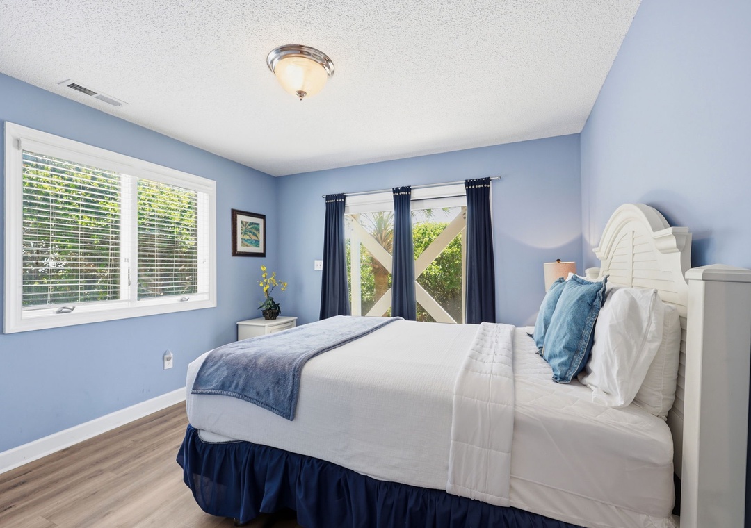 Picture yourself relaxing in this tranquil bedroom, where calming blue walls and crisp white linens create your perfect coastal retreat. Natural light streams through the windows, inviting gentle breezes and views of tropical greenery just outside.