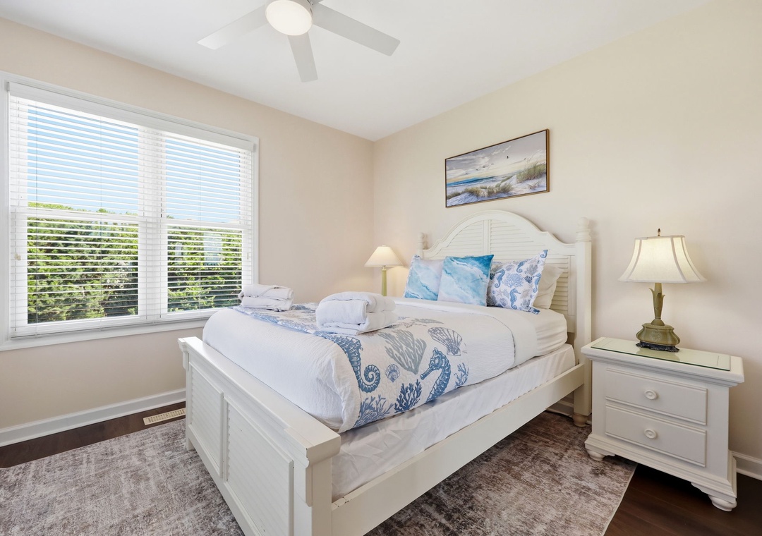Drift off in this serene coastal-themed bedroom, where soft linens and gentle seaside accents invite your most restful nights. The ceiling fan keeps you cool, while natural light and beach-inspired decor create a calming retreat.