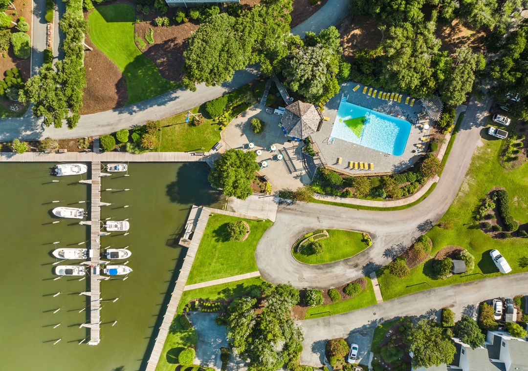 Aerial view of waterfront property featuring swimming pool, marina with boat slips, and landscaped grounds surrounded by lush greenery.