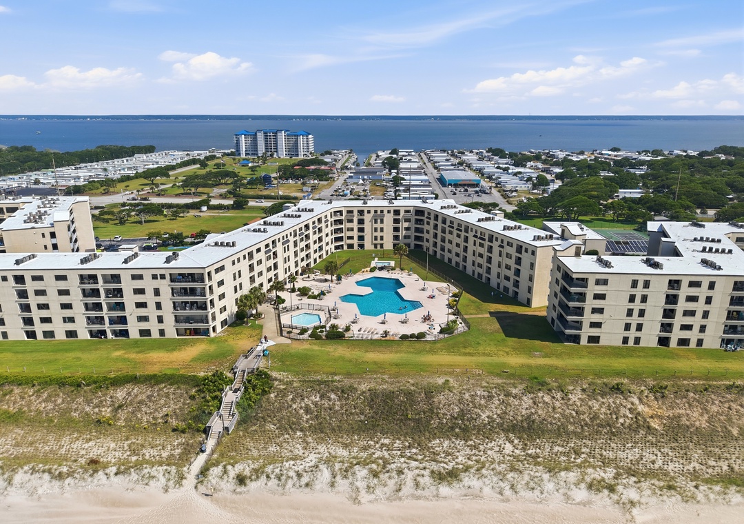 Beachfront vacation rental property featuring a central pool courtyard, direct beach access via boardwalk, and expansive bay views on a scenic coastal stretch.